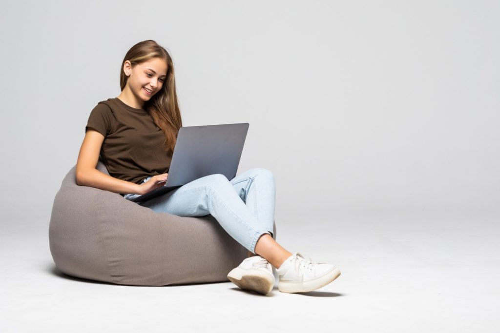 Young woman sitting on a bean bag chair, smiling while working on her laptop, representing a professional SEO consultant.