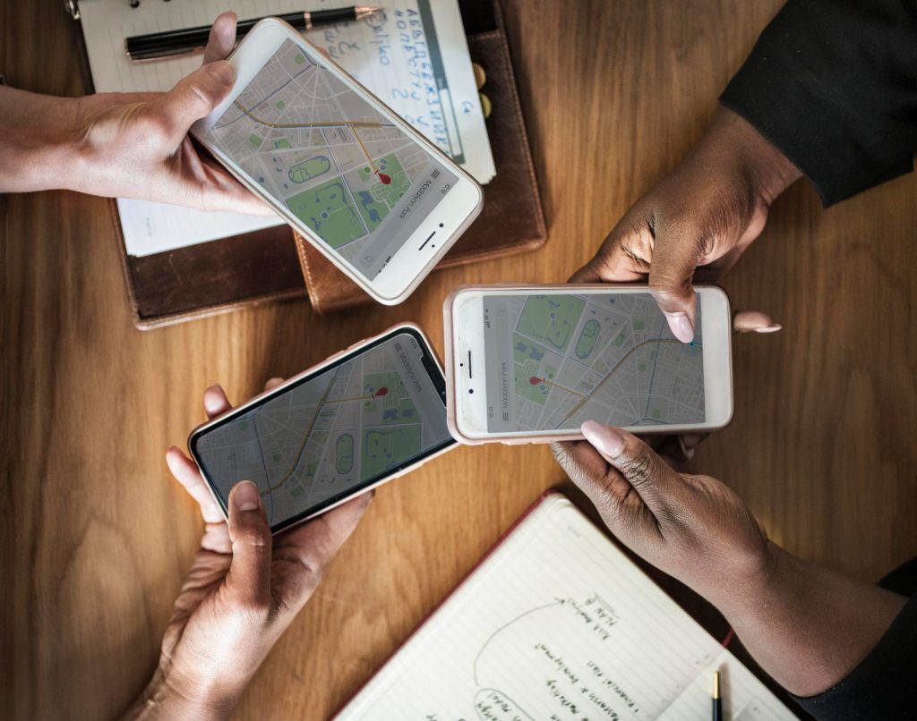 Three people holding smartphones displaying maps, discussing location-based business strategies.