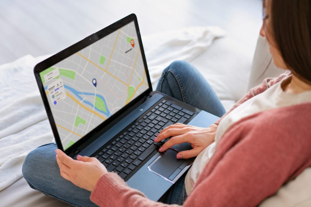 A woman sitting with a laptop, looking at a map, planning a route or searching for a local business.